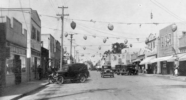 A vintage street scene with early 20th-century cars, buildings, and hanging decorations.
