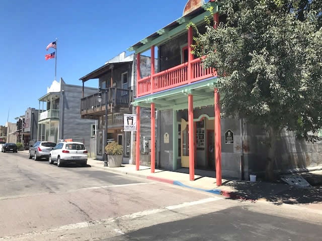 Street view of a small town with colorful buildings, parked cars, and American flags.