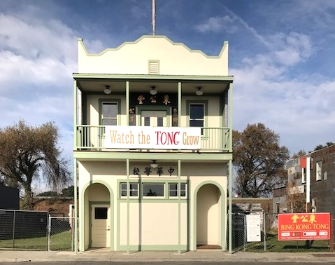 Two-story building with a sign that reads "Watch the TONG Grow" and a "BING KONG TONG" sign on the side.