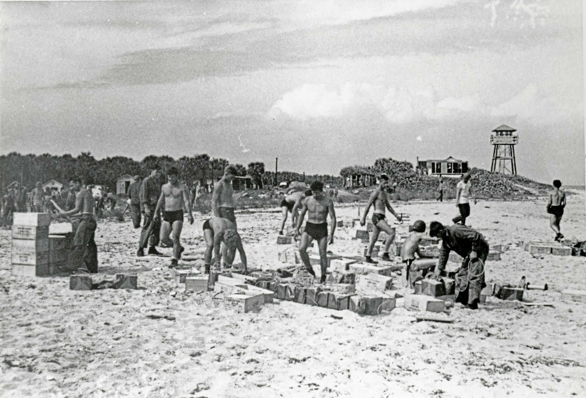 military service men working to move supplies on the beach with the tower in the background