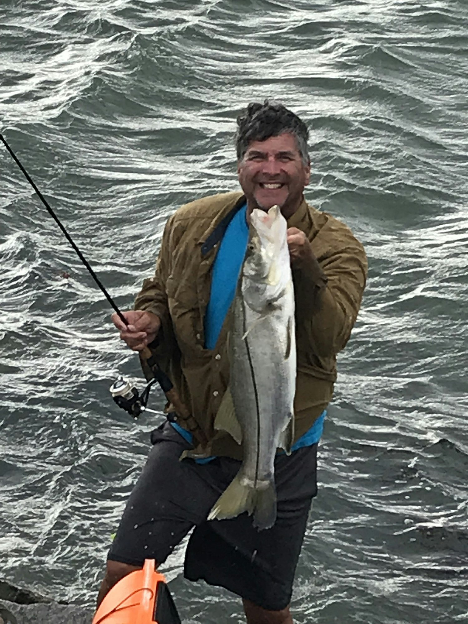 Man holding fishing rod and fish with water in the background