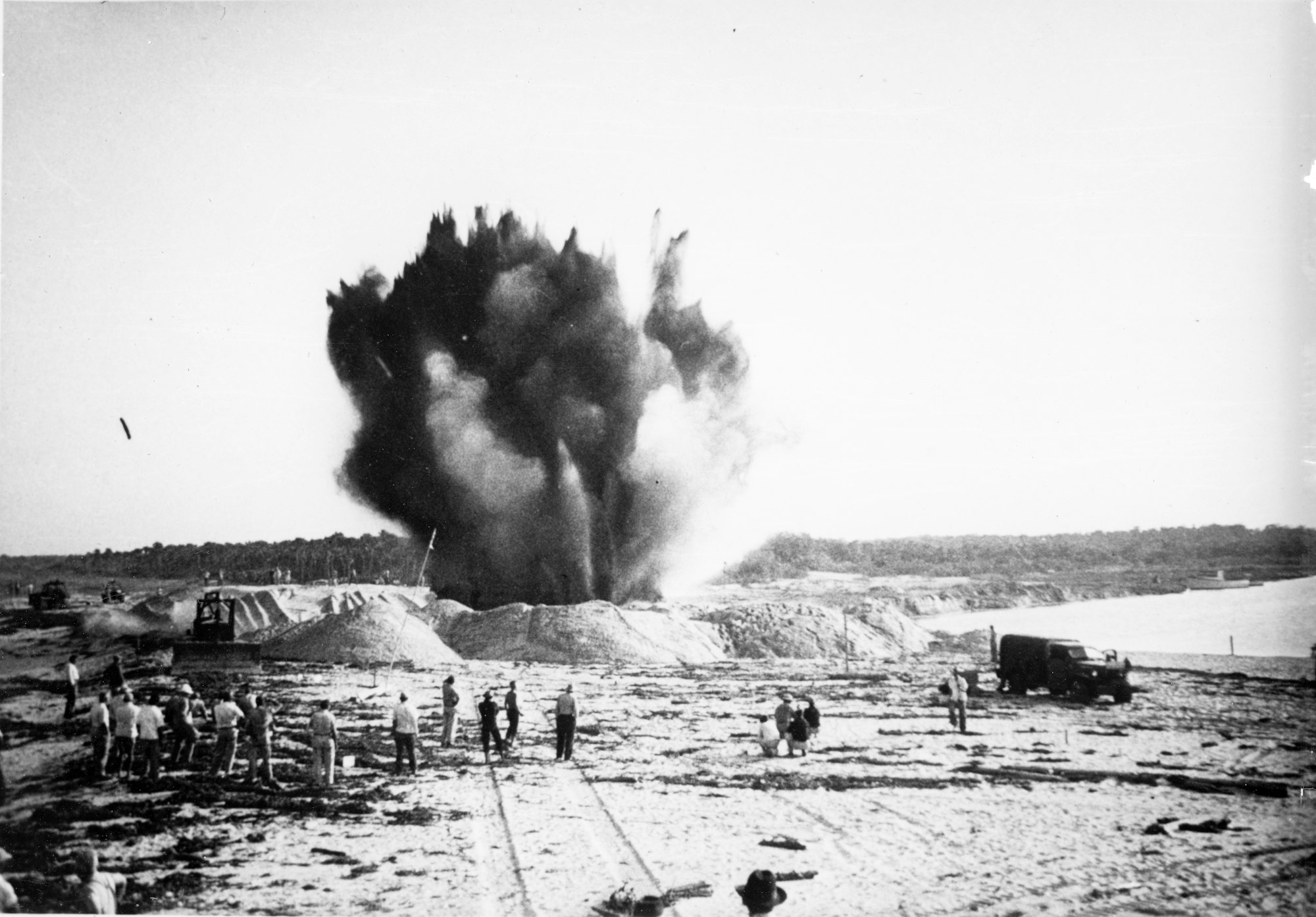 Wide view of dynamite blast of the last plug of sand between the Indian River and waters of the Atlantic Ocean with construction crews looking on