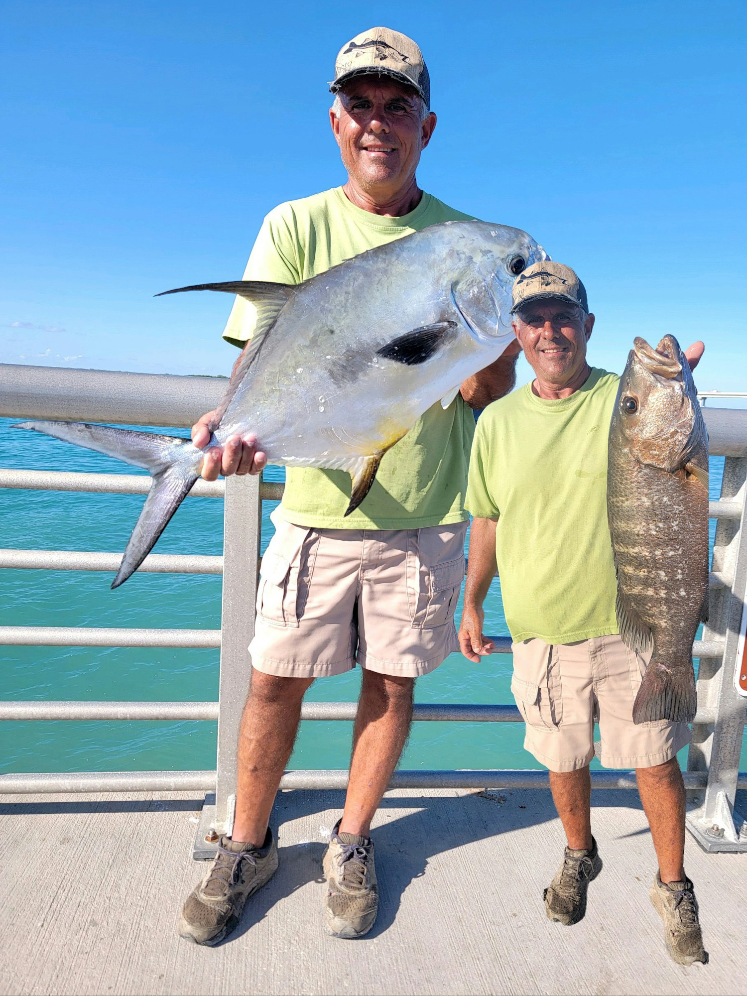 Two people holding large fish by the ocean.