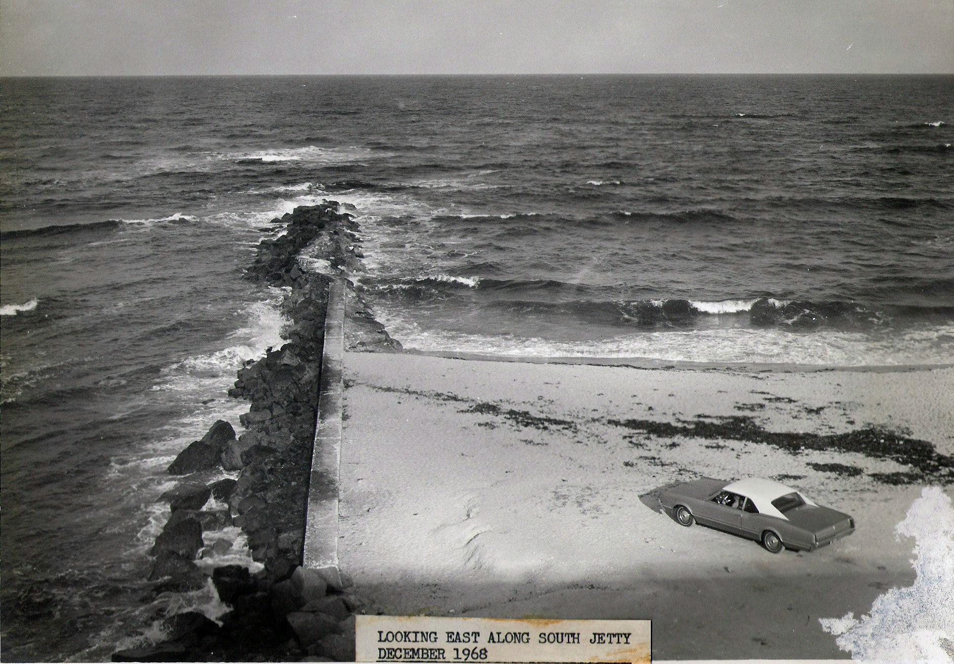 1968 view of south jetty looking East with car on beach shore at base of jetty