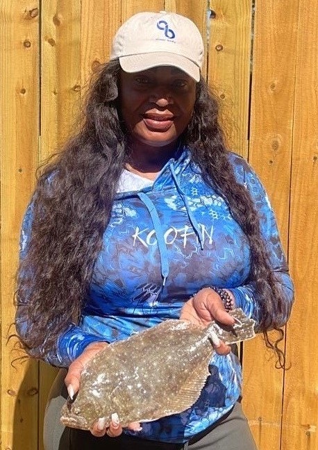 A person in a blue hoodie and cap holding a fish in front of a wooden fence.