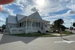White house with porch, person on street, sunny day, partly cloudy sky.
