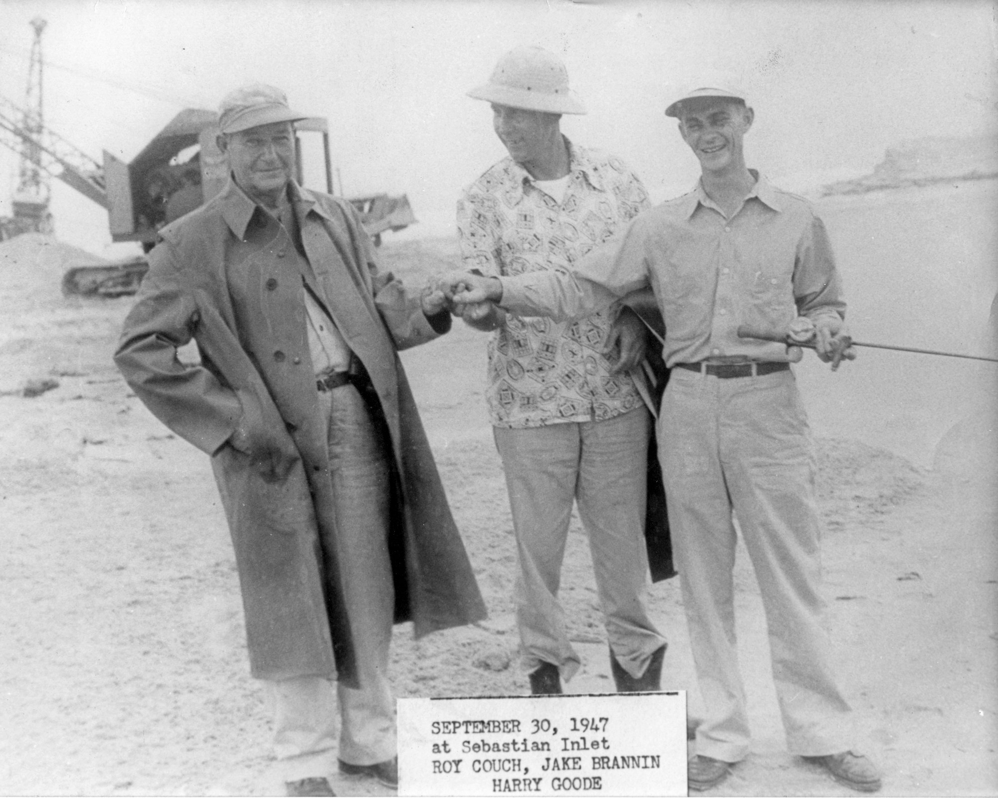 Three men standing together with an excavator in the background from 1947