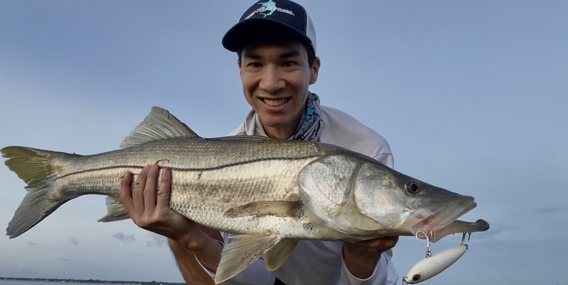 A person holding a large fish with a fishing lure, smiling at the camera.
