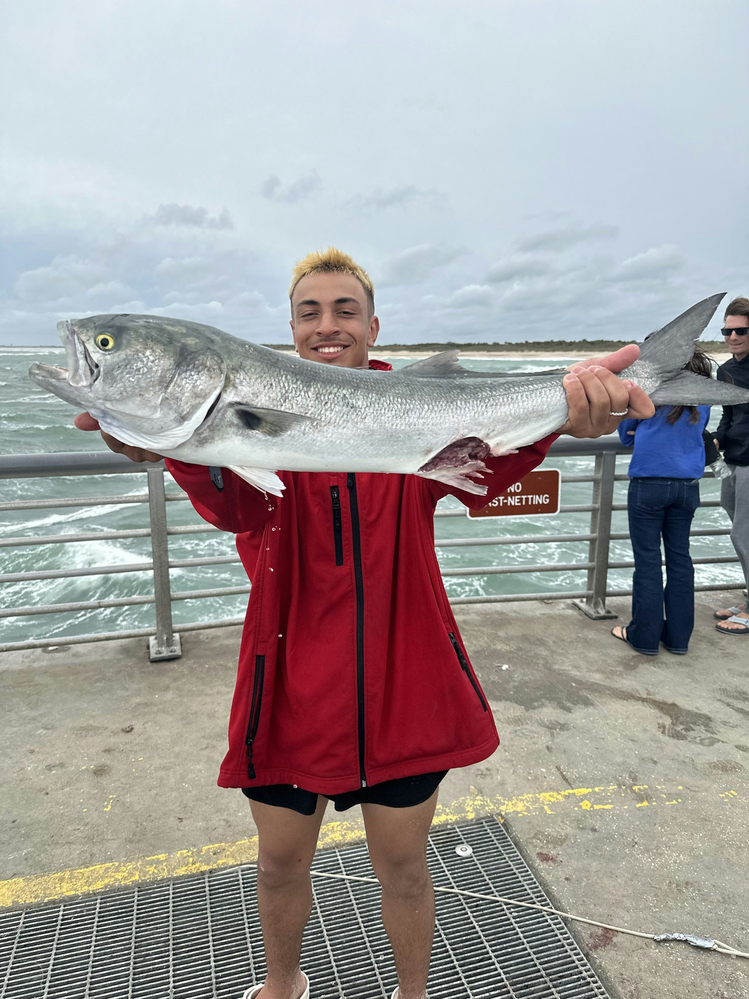 A person holding a large fish with the ocean in the background. (Image is rotated)