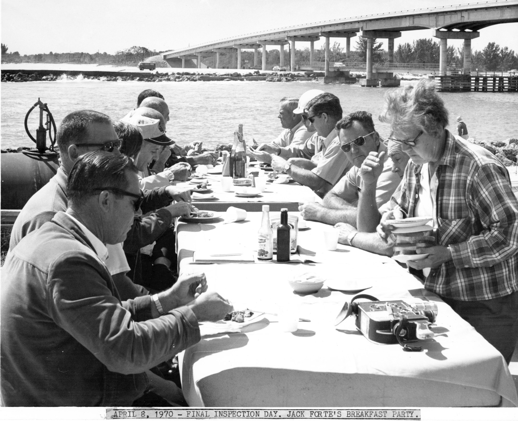 people gathered at a table for a meal with Sebastian Inlet bridge in background