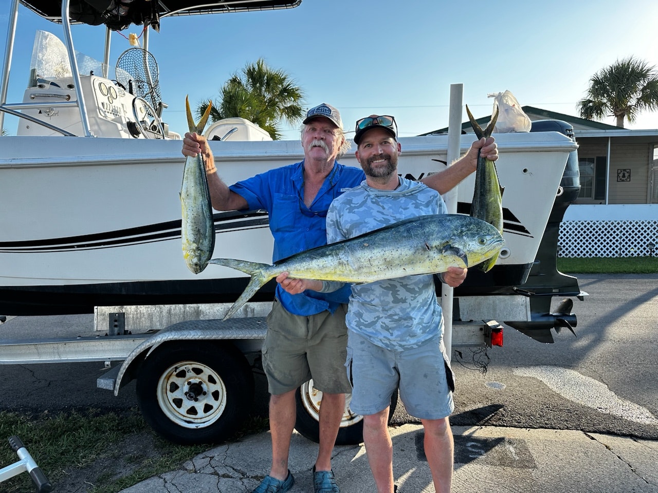 Two men holding large fish in front of a boat on a trailer.