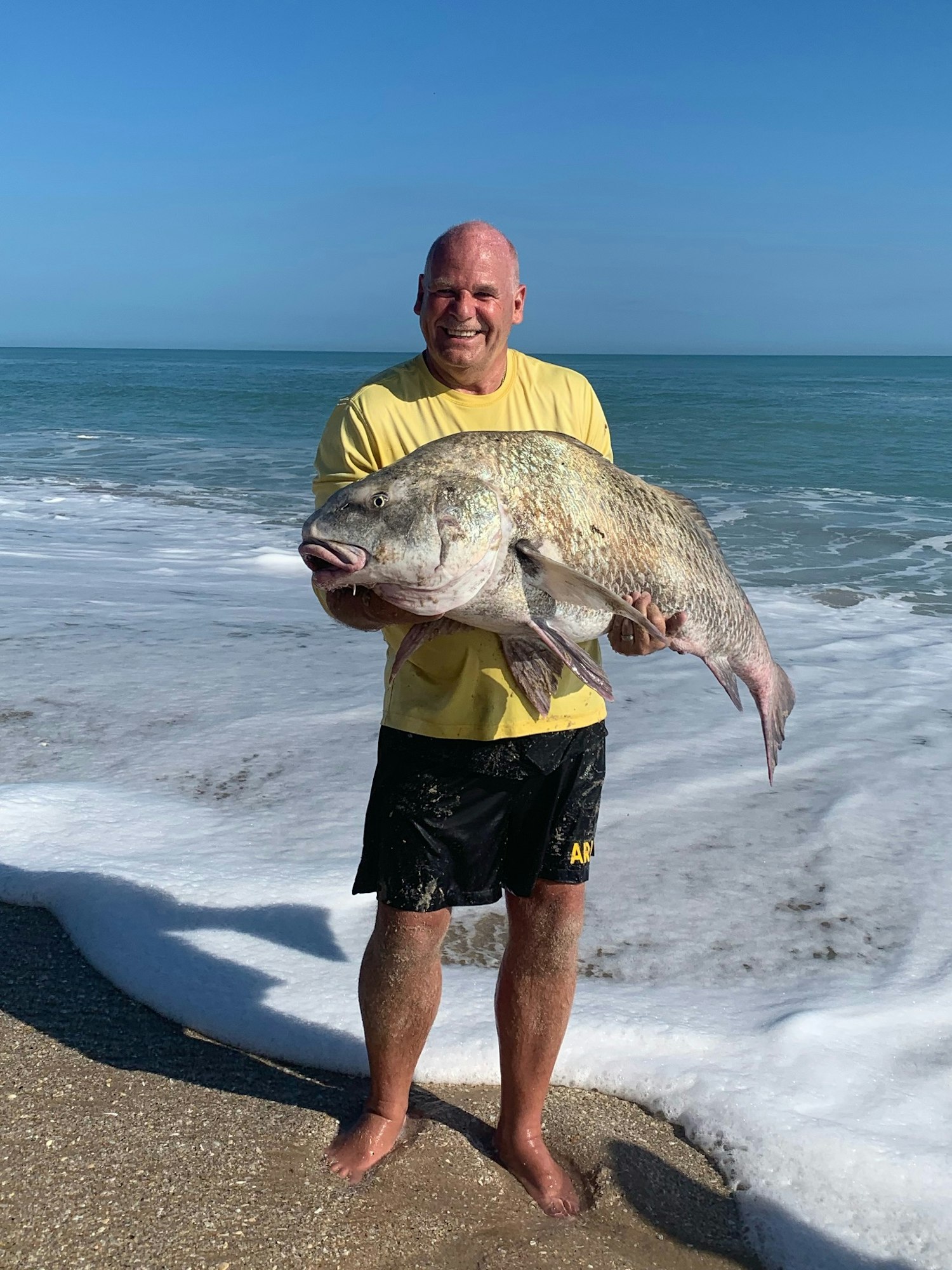 man holding large fish standing in surf on beach