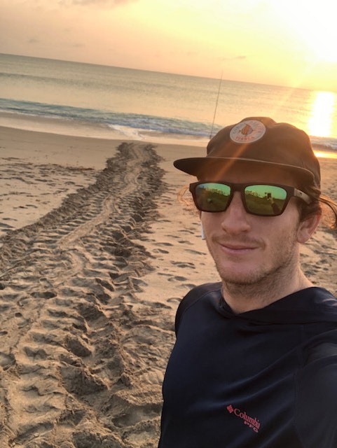 Selfie of man with sunglasses by sea turtle nesting tracks on beach at sunrise