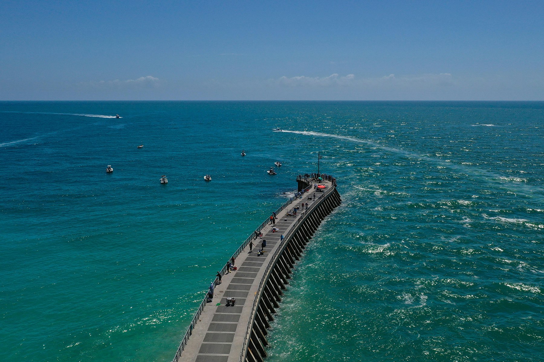 aerial view of jetty jutting out into sea with fisherman on pier and boats surrounding