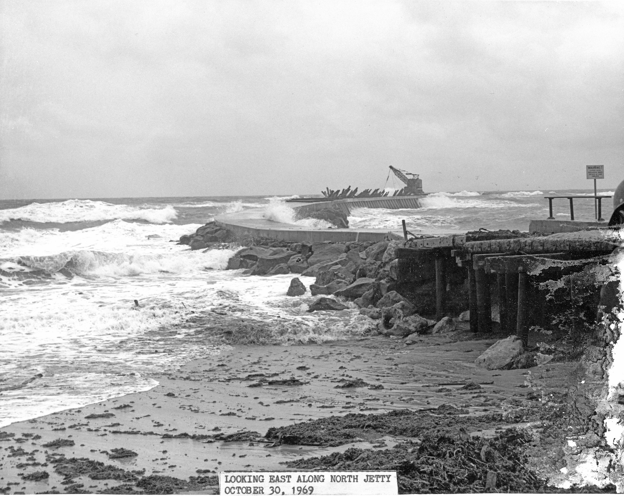 looking out from the base of north jetty with rough seas, damage to the jetty and crane stranded out on the tip