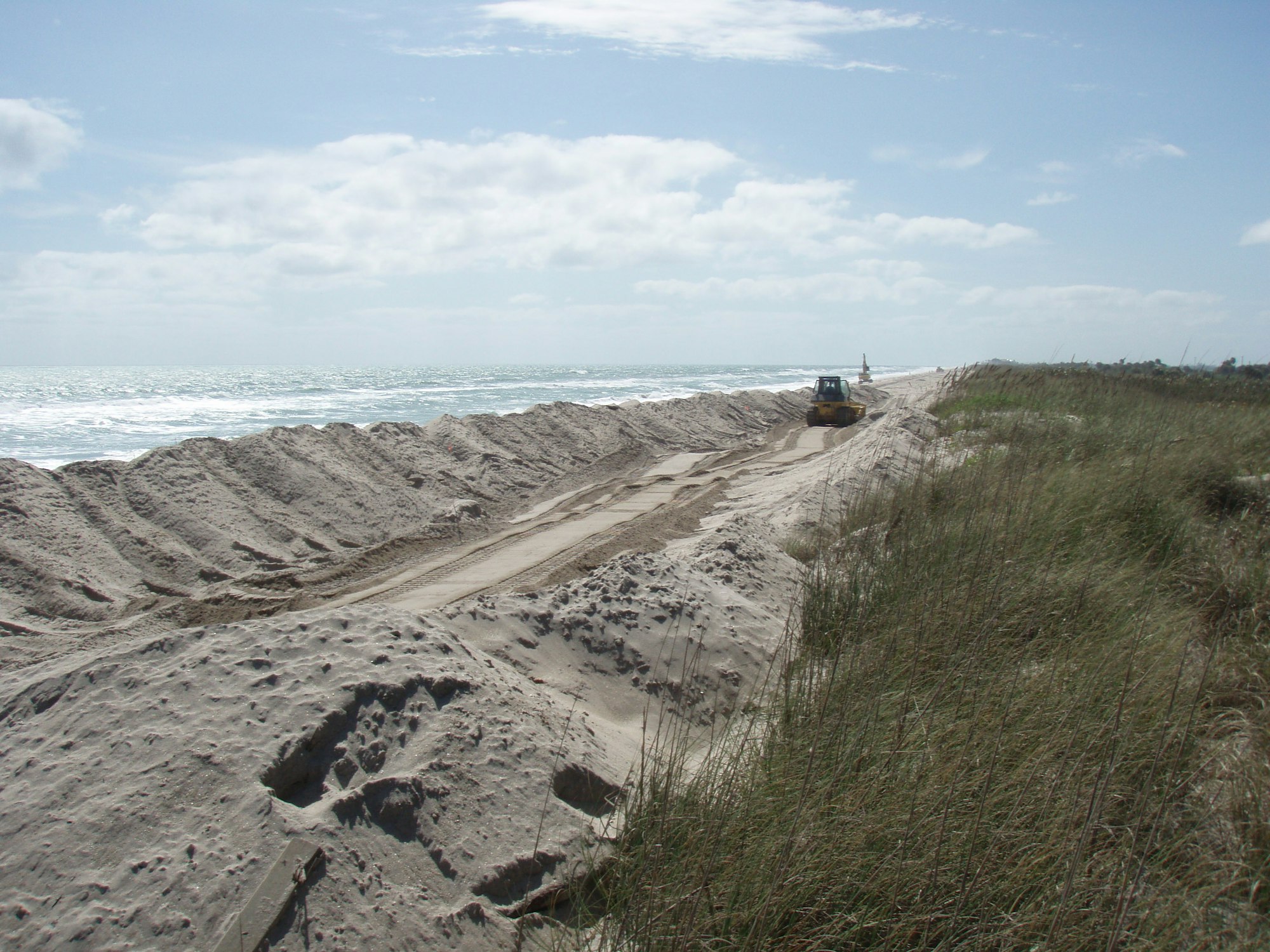 bulldozer in distance shaping mounds of sand placed on beach