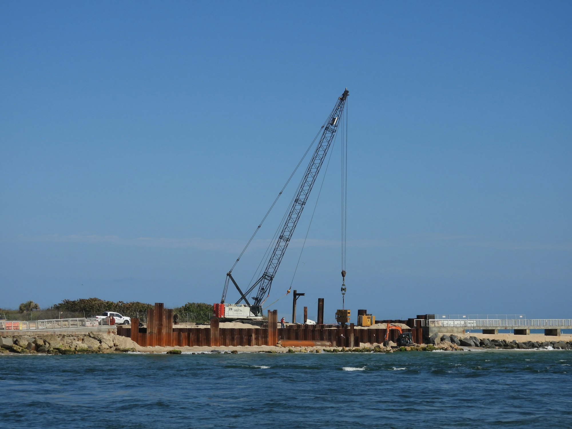 A construction site near the water with a crane and metal structures.