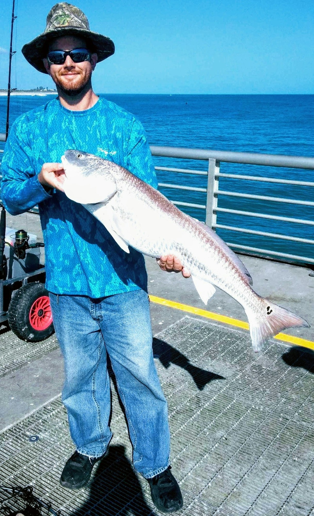 man on jetty wearing hat holding a fish