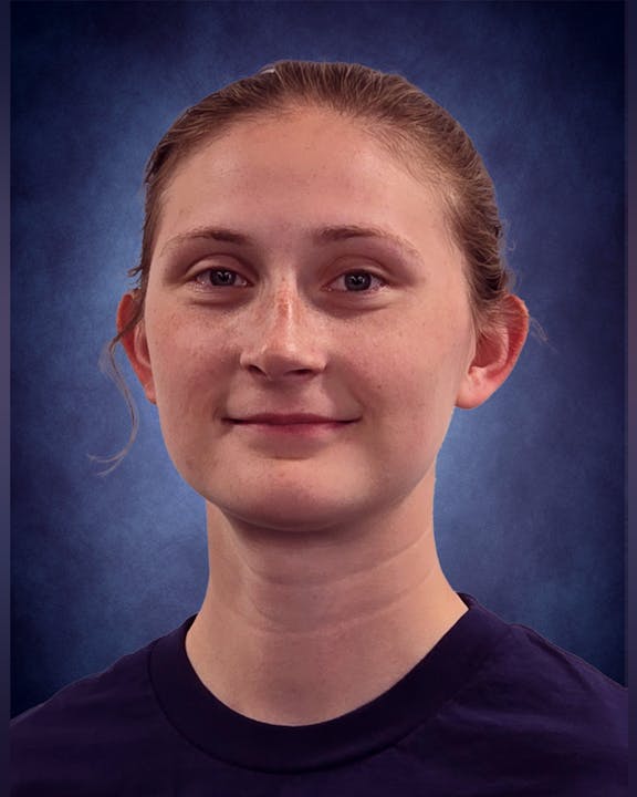 A portrait of a person with light brown hair in a ponytail, wearing a dark top, against a blue background.