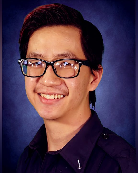 A person wearing glasses and a dark shirt smiles in front of a blue background.