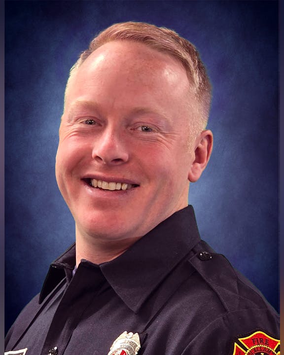 A person in a uniform, smiling, with a badge and shoulder patch visible.