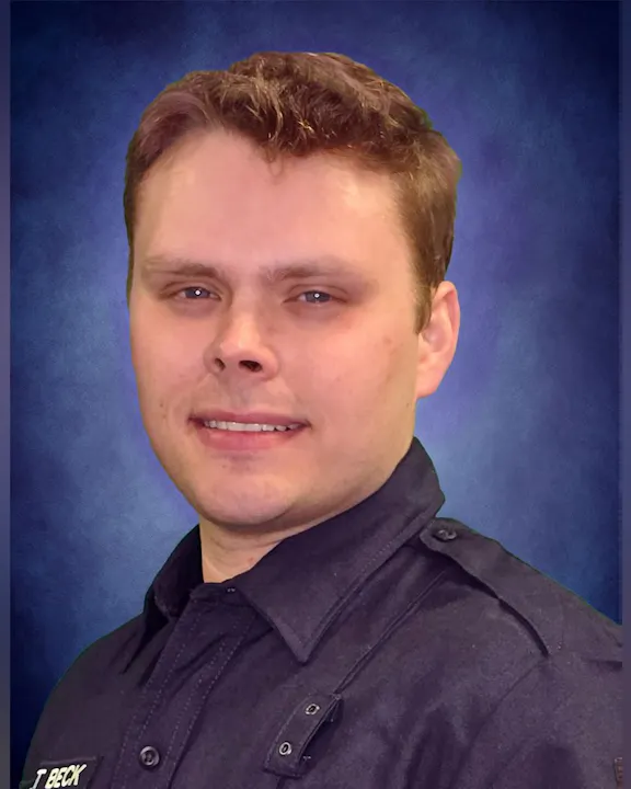 A man in a uniform smiles at the camera, with a blue background enhancing the image.