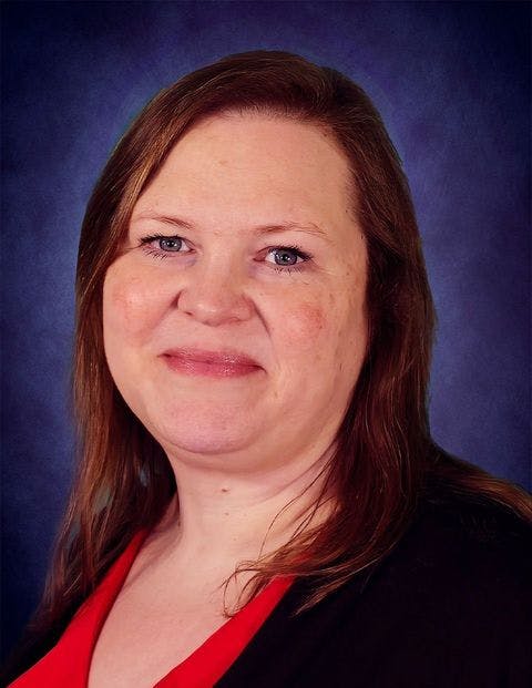 A woman smiling against a blue background, wearing a red top and black cardigan.