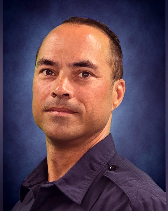 A man in a dark shirt against a blue textured background.