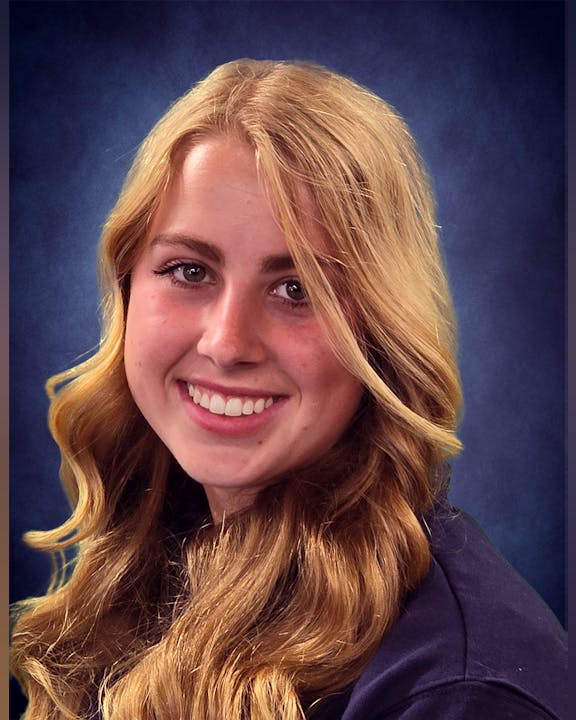 A person with long blonde hair smiling against a blue background.
