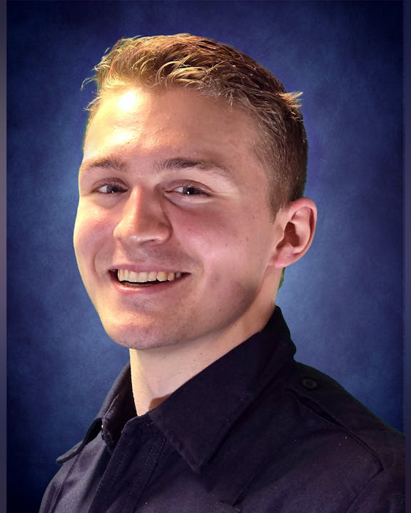 A smiling person in a dark shirt poses against a blue background, conveying a friendly and approachable demeanor.