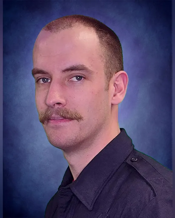 The image features a man with a closely cropped hairstyle and a mustache, wearing a dark uniform with a blue background.