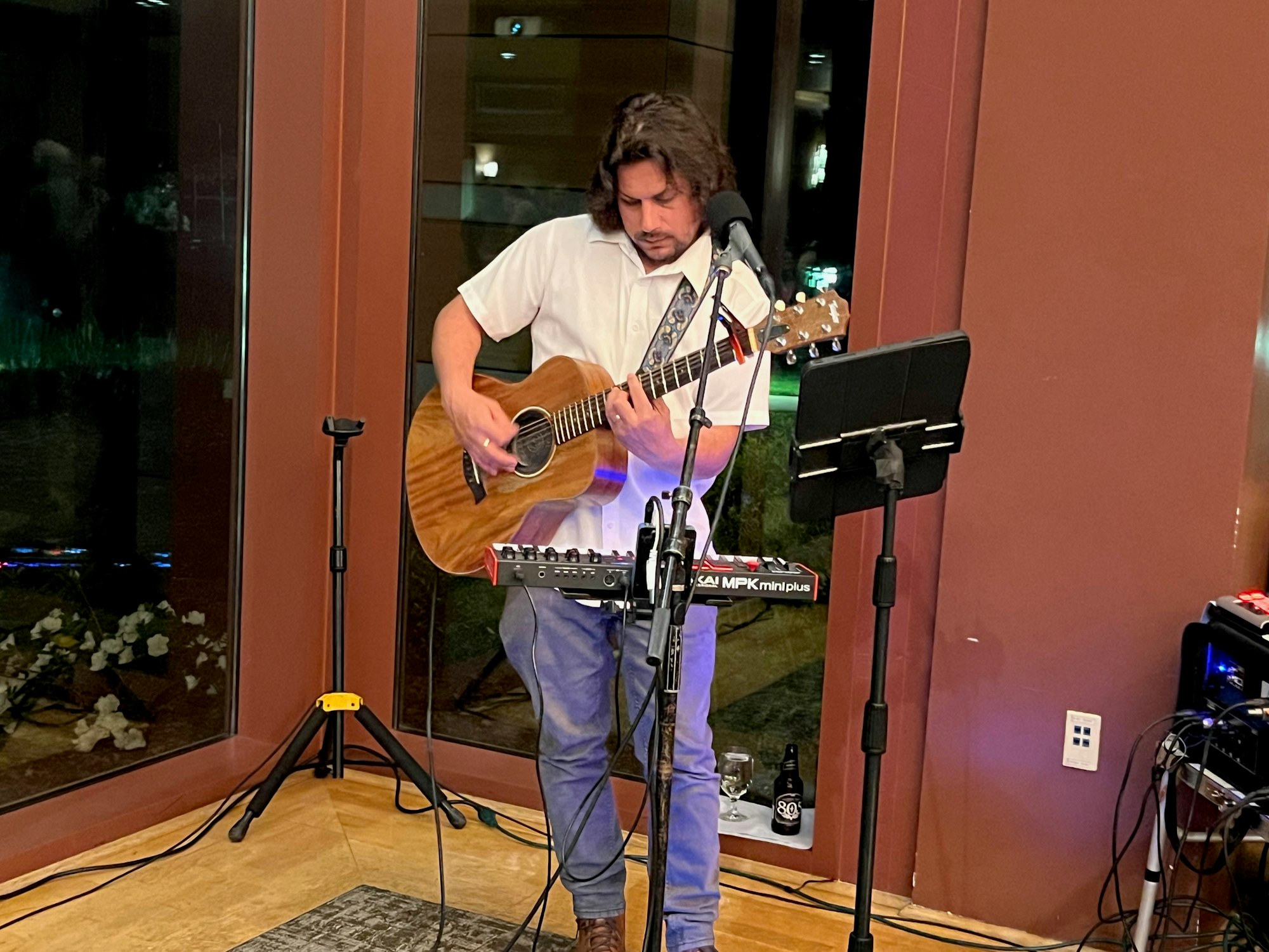 A person playing an acoustic guitar with a microphone and music stand, performing indoors.