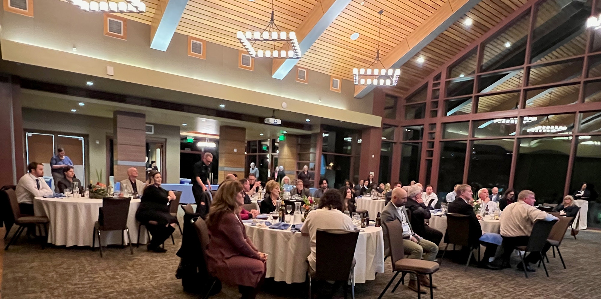 A formal event with people seated at round tables in a large room with high ceilings and windows.
