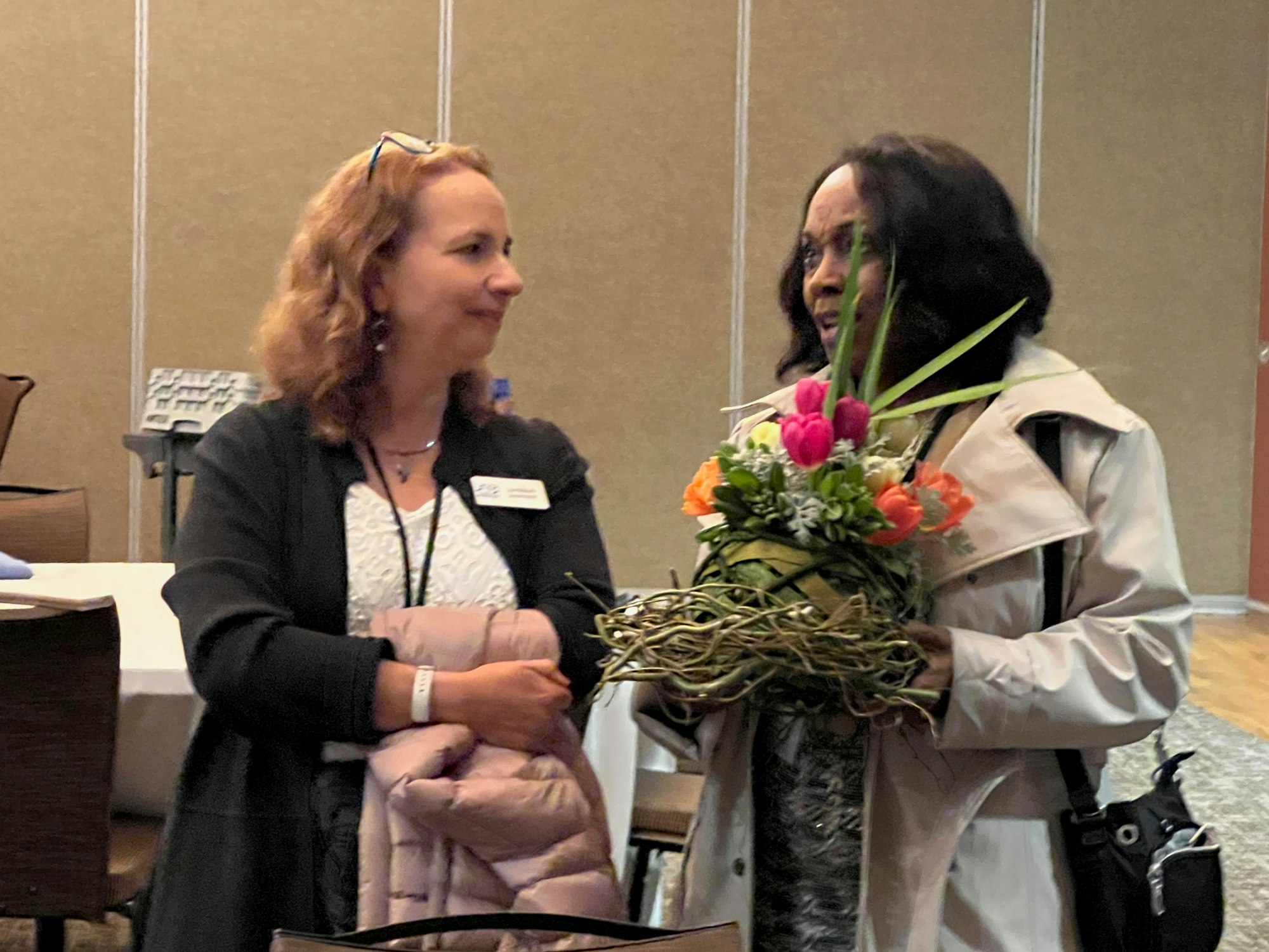 Two people talking, one holding a flower arrangement.
