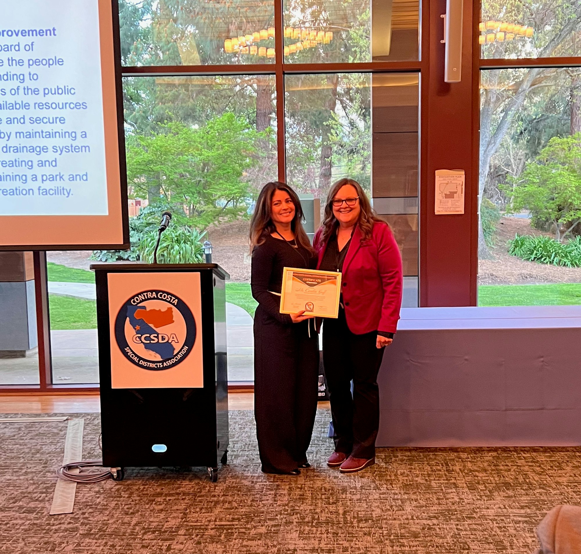 Two people posing with a certificate at an event; a podium with a "Contra Costa Special Districts Association" logo is nearby.