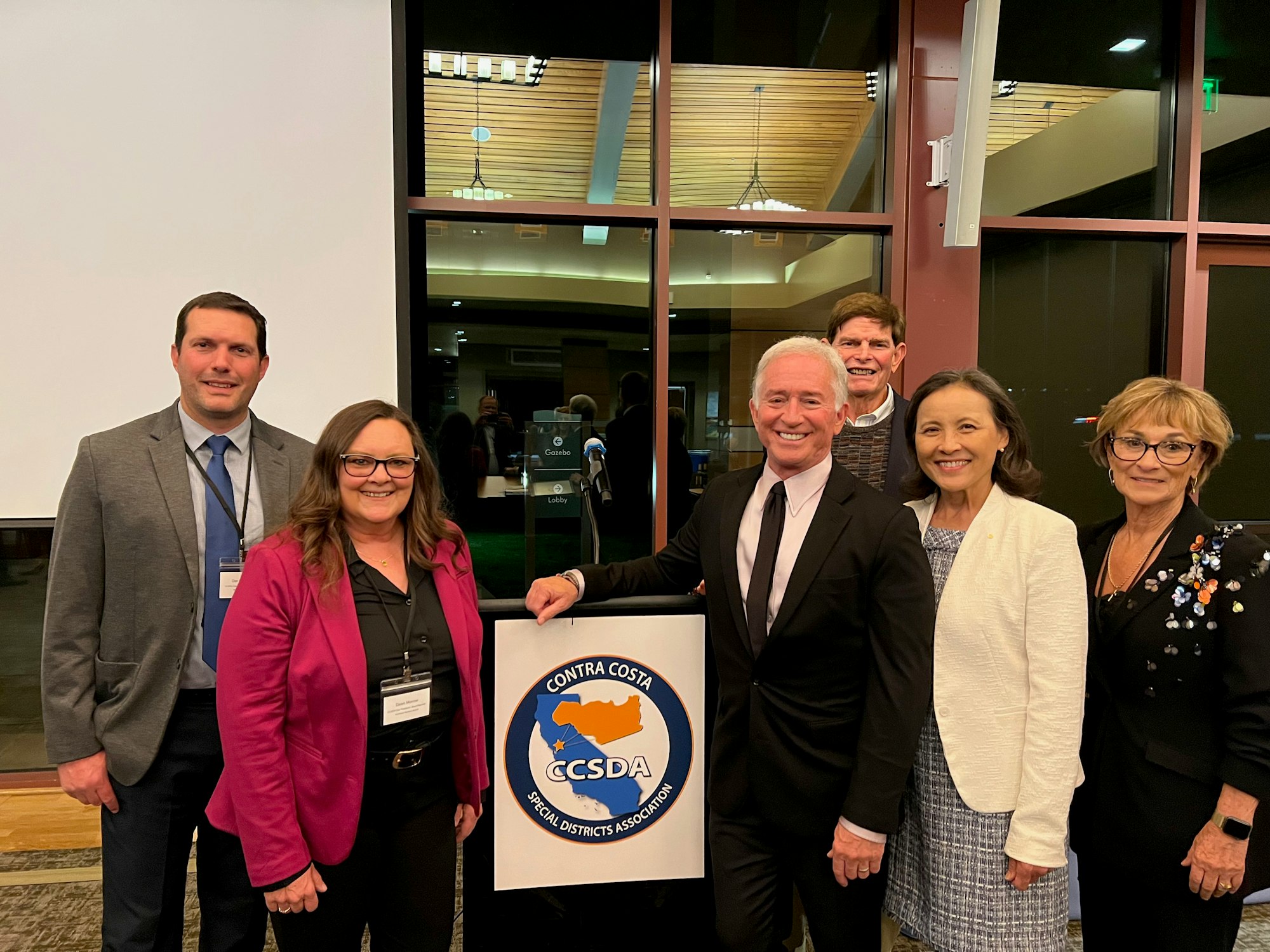 A group of six people posing with a "Contra Costa Special Districts Association" sign indoors.