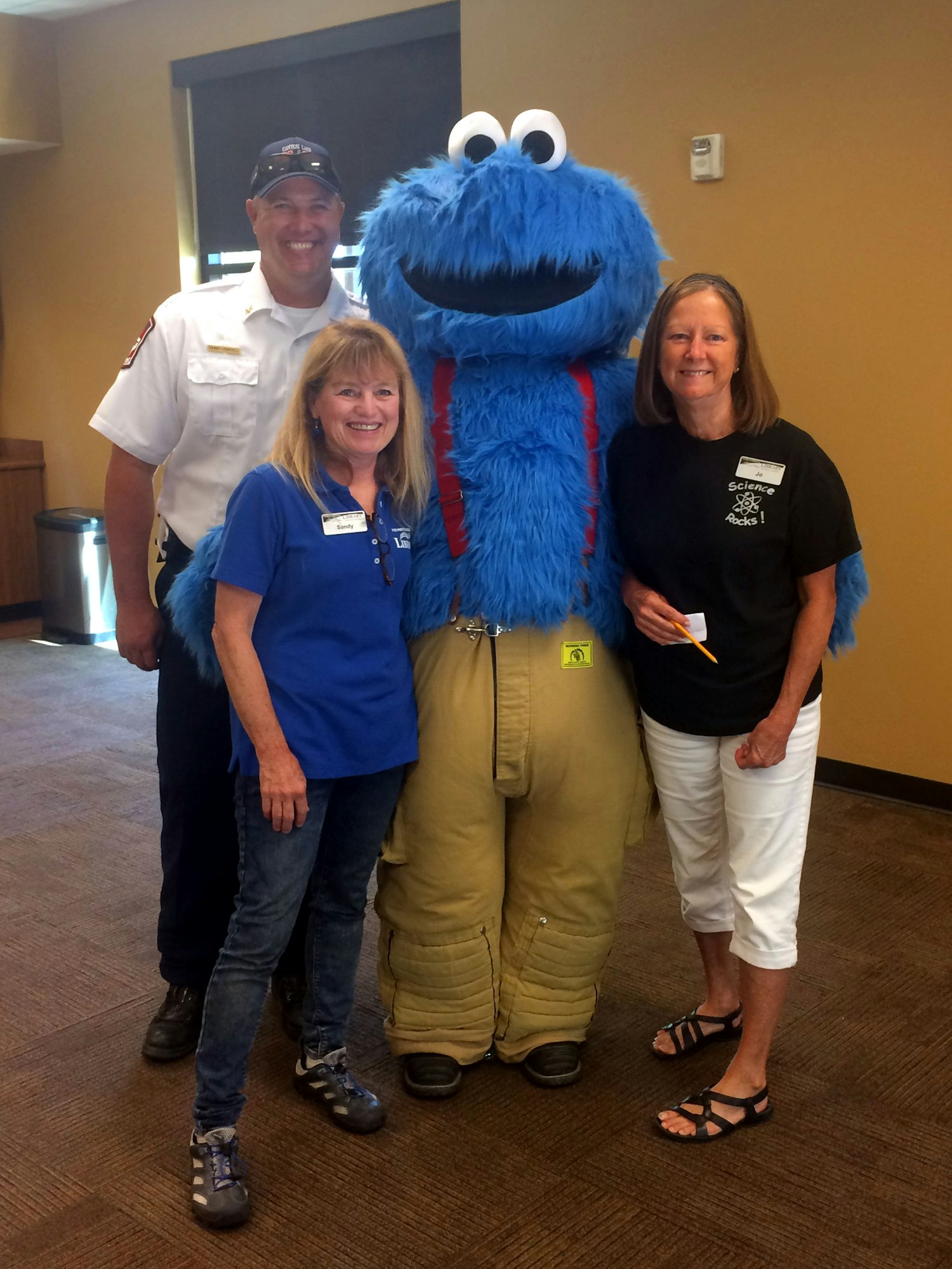 Three people and a person in a blue furry costume are smiling for a photo inside a room.