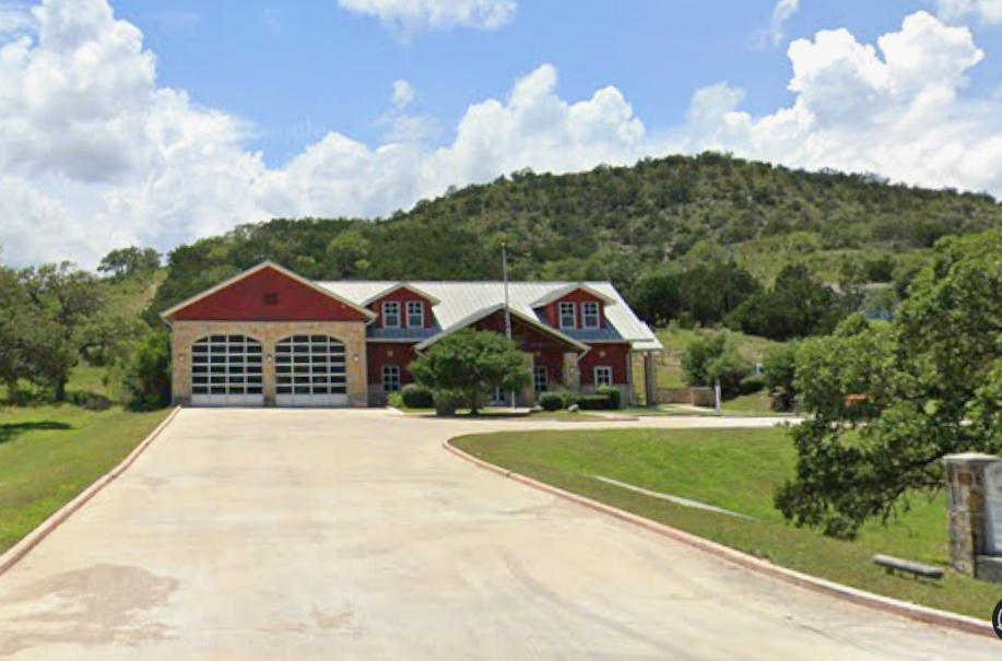 A red and stone house with a metal roof, large garage doors, and a landscaped driveway, set against a hillside with trees.