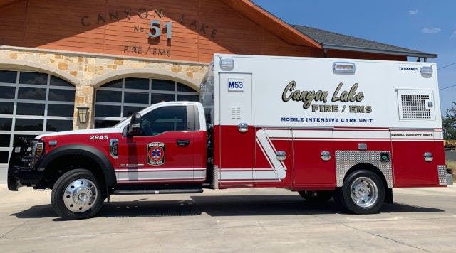 A red and white Canyon Lake Mobile Intensive Care Unit ambulance parked in front of a fire station.