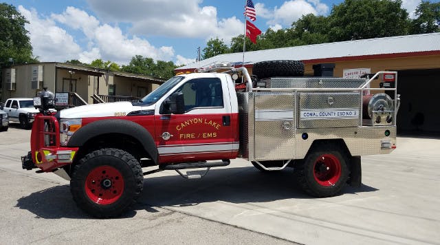 A Canyon Lake Fire/EMS truck parked outside a station with an American flag in the background.