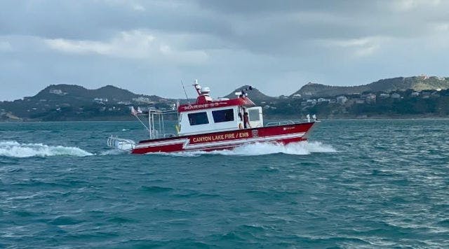 A red and white fire rescue boat speeding across the water with hills in the background.