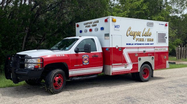 A red and white Canyon Lake Fire/EMS ambulance parked on a roadside with trees in the background.