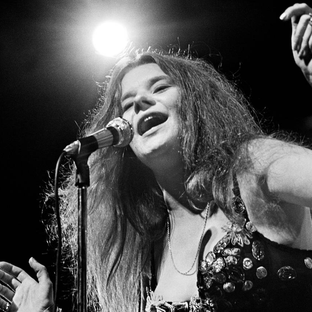 A black and white photo of a woman singing into a microphone on stage, with a spotlight above her.