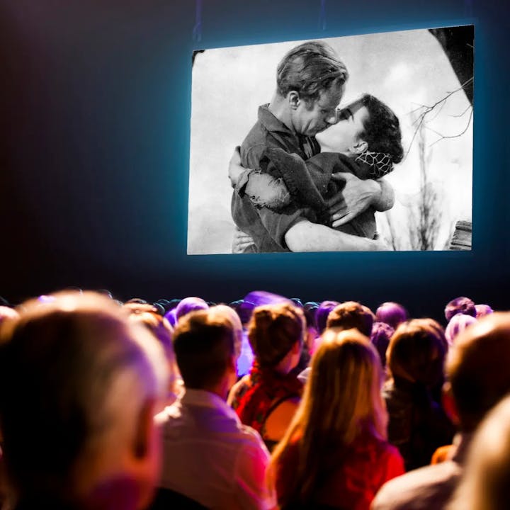 Audience watching a black and white film of a couple kissing.