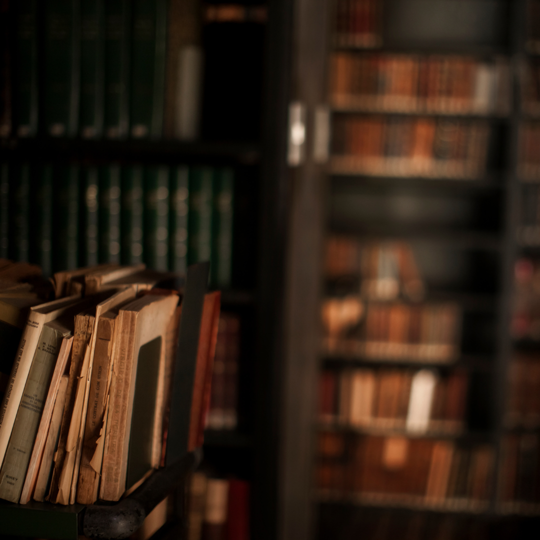 Old books on a library shelf, with some in a book holder.