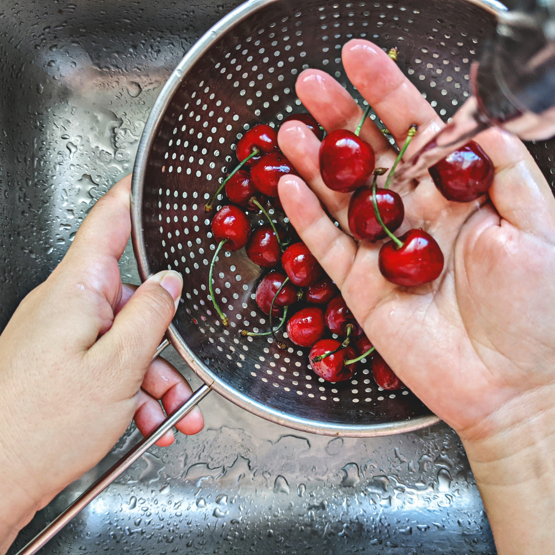 A person is washing fresh red cherries in a colander under running water.