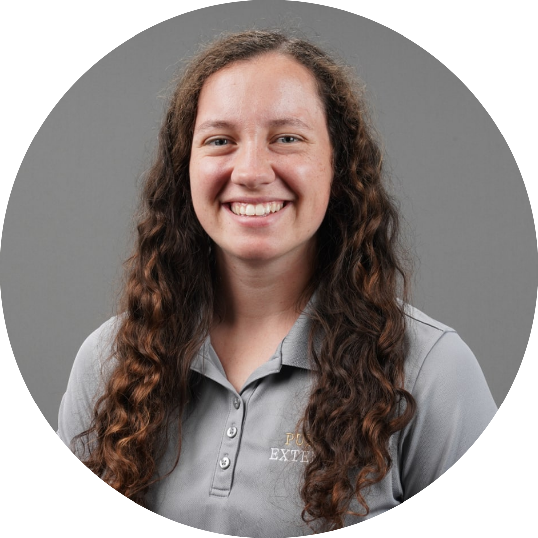A smiling person with long curly hair wearing a gray shirt, posed against a neutral background.