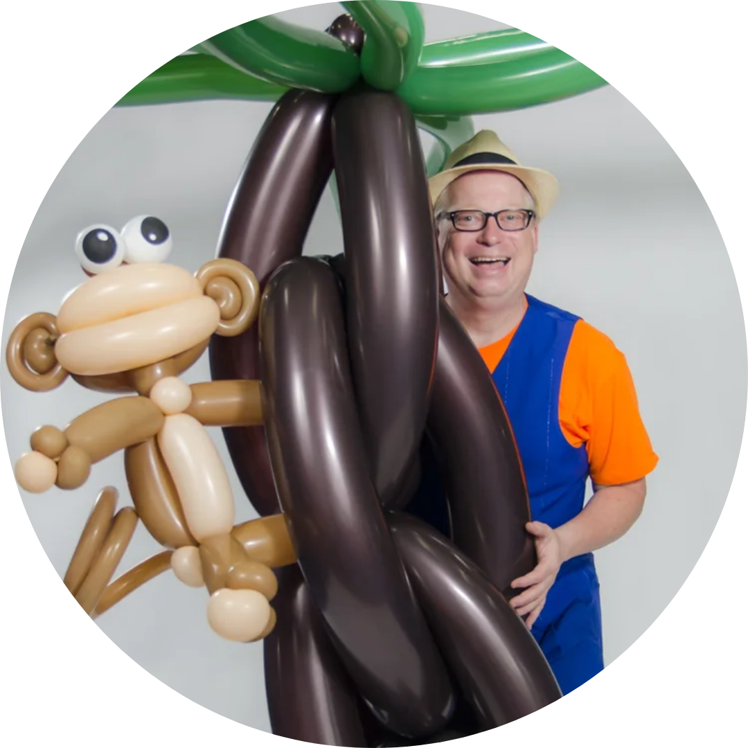 A person in a colorful outfit poses with a balloon creation of a monkey and tree.