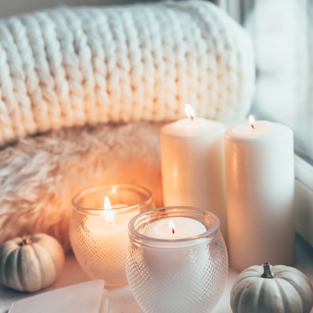 Cozy setting with lit candles, mini pumpkins, a knitted blanket, and fluffy textures.