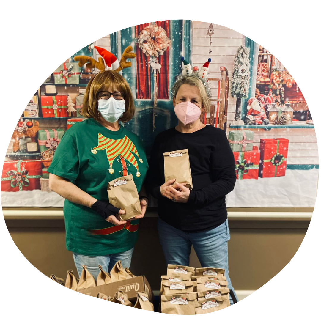 Two people with masks, holiday backdrop, holding paper bags.